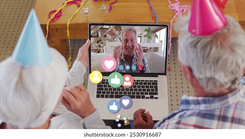 Senior couple having a video call celebration. They are wearing party hats and interacting with a man on the laptop screen. - Powered by Shutterstock