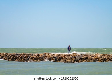 Senior Man In Jacket And Blue Jeans Walking Along Jetty Of Rocks On A Bright, Breezy Afternoon In Winter Along The Gulf Coast Of Southeast Florida, USA, With Digital Oil-painting Effect. 3D Rendering.