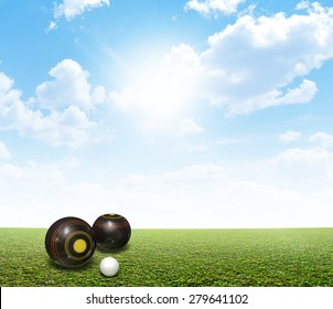 A set of wooden lawn bowls next to a jack on a perfect flat green lawn against a blue sky with white clouds