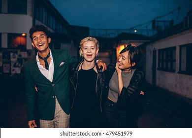 Shot Of Young People Walking On The City Street In Evening And Laughing. Three Young Friends Having Fun On City Street At Night.