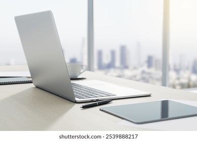 Side view on sunlit workspace table with modern light grey laptop, digital tablet and coffee cup on big window background with city view. 3D rendering