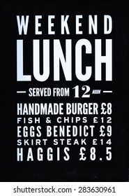 Sign Of White Lettering On Blackboard Saying Weekend Lunch, Served From 12 Noon, Handmade Burger, Fish & Chips, Eggs Benedict, Skirt Steak, Haggis