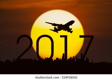Silhouette of airplane flying in the sky above numbers 2017 and city with a golden sun, shot at sunset time