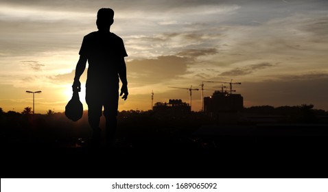 Silhouette Of A Construction Worker Walking Home With His Pack Dinner In The Evening For The Concept Of Urban Migrant Worker. 