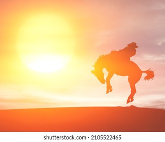 Silhouette Of A Cowboy Wrestle A Bucking Bronco Horse Against A Surreal Sunset Sky.