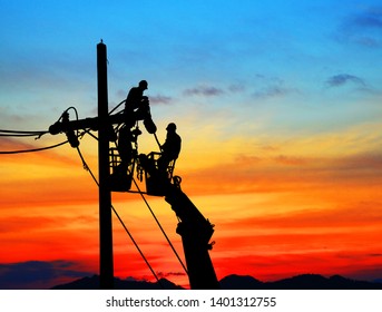 Silhouette Electrical Engineers Working On Electricity Pylon High Tension Power Line Repairs And Maintenance  On Blurry Sunset Background