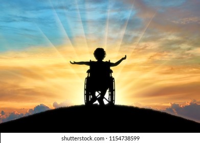 Silhouette Of A Happy Disabled Child Girl Sitting In A Wheelchair Atop A Hill At Sunset. Concept Of Happy Children With Disabilities