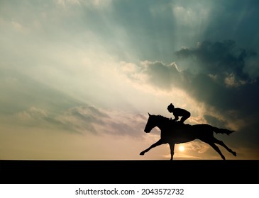 Silhouette Of A Jockey Racing A Racehorse On A Race Track Against A Surreal Sunset Sky.