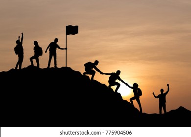 Silhouette of people helping each other hike up a mountain and celebrating at sunset background. Business, teamwork, success, help and goal concept.