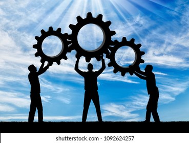 Silhouette Of The Three Men Holding The Gears Put Them Together In One Gear. The Concept Of Mutual Benefit