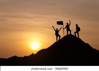 Silhouette of three people are celebrating success at the top of the mountain, sky and sun light background. Business, successful, leadership, achievement, teamwork and goal concept.
