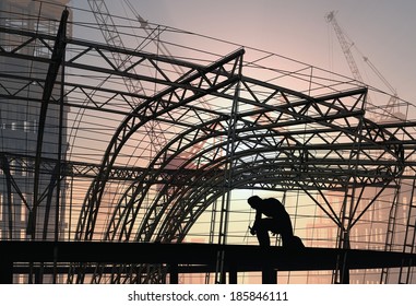 Silhouette of a welder and a building structure.