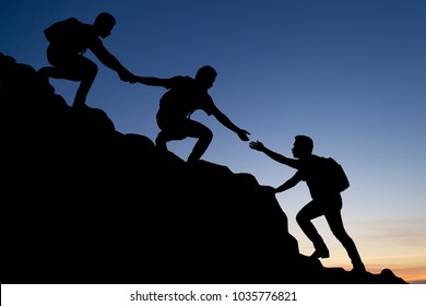 Silhouette of young man helping each other hike up a mountain at sunrise. Business, teamwork, goal, success and help concept. 