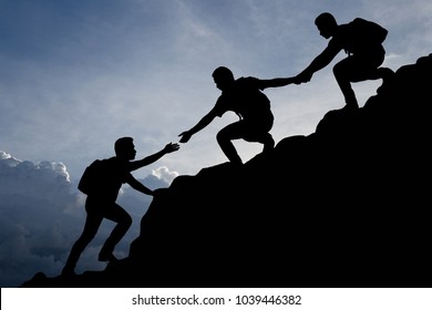 Silhouette of young man helping each other hike up a mountain at sunrise. Business, teamwork, goal, success and help concept. 