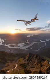 Small plane flying over a mountain valley at sunset with winding rivers, dramatic sky, and 3d Rendering; Background from BC Canada.