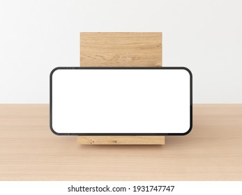 Smartphone Frame With Blank White Display Standing On The Side, Landscape, On Wooden Stand On Natural Wooden Table With White Background. Realistic Smartphone Mockup. 3D Illustration