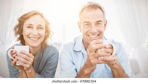 Smiling middle aged couple sitting on the couch having coffee looking at camera at home in the living room - Powered by Shutterstock