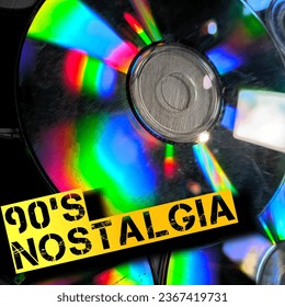 A stack of colorful CDs with rainbow colors reflecting off of them. The CDs are all different sizes and shapes, and they are all sitting on top of each other. “SHOTLIST1990” 