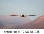 A state-of-the-art military drone with expansive wings maneuvers above a desolate desert, navigating near distant mountains under a vividly clear sky.