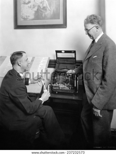 Stock brokers with a new box shaped stock ticker in\
May 1929.