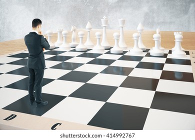 Strategy concept with thinking businessman and white chess pieces standing on huge chessboard with concrete wall in the background. Sideview, 3D Rendering