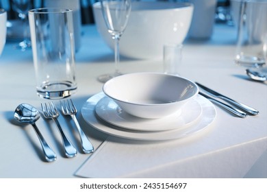 Sumptuously laid dining table featuring polished silver cutlery, sparkling crystal glasses, and elegant white porcelain plates, poised for a sophisticated banquet or gala.