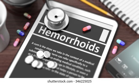 Tablet with "Hemorrhoids" on screen, stethoscope, pills and objects on wooden desktop.