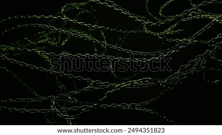 A tangle of metal chains hangs in the darkness, their links shimmering with a green glow.
