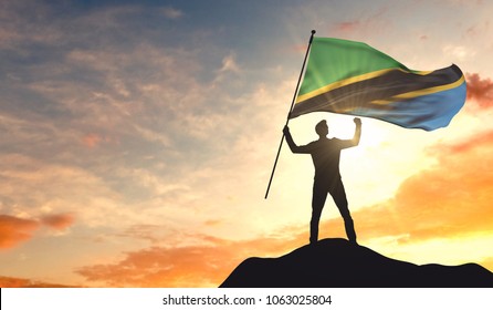 Tanzania flag being waved by a man celebrating success at the top of a mountain. 3D Rendering