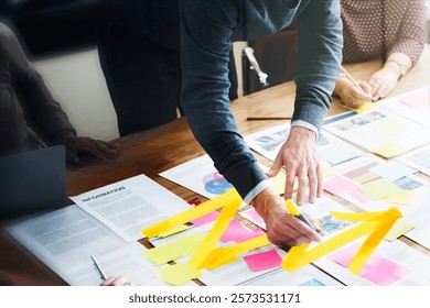 Team collaborating on project with sticky notes and documents. Hands pointing at notes, teamwork in action. Creative brainstorming with colorful sticky notes.