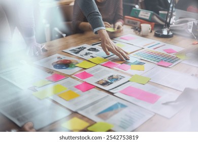 Team collaborating over documents and sticky notes on an office table. Hands reaching in for business brainstorming ideas, planning, and organizing tasks. - Powered by Shutterstock