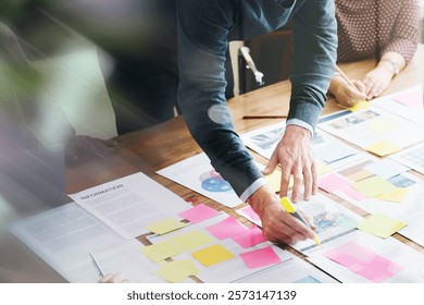 Team collaborating with sticky notes and documents on a table. Hands pointing and writing, planning ideas, teamwork in action, creative brainstorming session. Business startup strategy and plan.