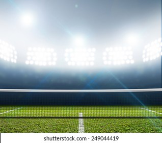 A Tennis Court In An Arena With A Marked Green Lawn Surface At Night Under Illuminated Floodlights