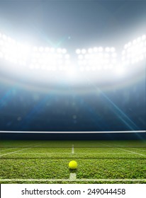 A Tennis Court In An Arena With A Marked Green Lawn Surface At Night Under Illuminated Floodlights