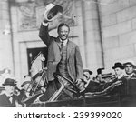 Theodore Roosevelt, waving his hat, as he stands in car. ca.1910.