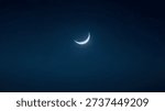 Thin crescent moon in deep blue night sky.