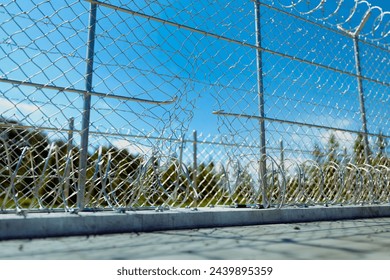 This image captures a detailed view of a damaged chain link fence, with serene blue sky and fluffy clouds in the background, highlighting concepts of security, vulnerability, and boundary breaches.