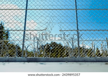 This image captures a detailed view of a damaged chain link fence, with serene blue sky and fluffy clouds in the background, highlighting concepts of security, vulnerability, and boundary breaches.