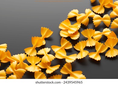 This image captures the essence of scattered, golden-hued, uncooked farfalle pasta, presenting a striking contrast on a dark surface, highlighting its texture and form. - Powered by Shutterstock