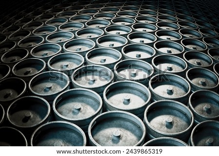 This image captures a vast collection of industrial metal kegs, neatly arranged in rows within a dim storage area, emphasizing the beauty of uniformity and industrial texture.