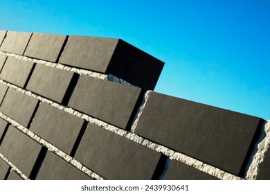 This image features meticulously stacked black slate tiles, their rugged textures contrasted sharply with the vibrancy of the blue sky overhead, illustrating materials in construction.