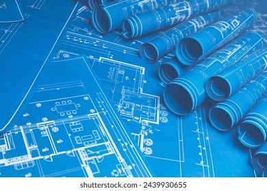 This image showcases a collection of detailed engineering blueprints, both rolled and flat, on a workspace, illustrating the intricate planning process for architectural and mechanical designs. - Powered by Shutterstock