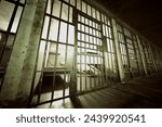 This stark image captures the haunting atmosphere of an abandoned prison cellblock, with long shadows and metal bars creating a profound sense of isolation and desolation.