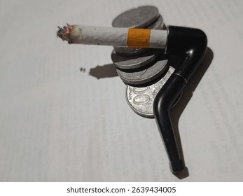 This striking image captures a unique intersection of traditional and modern smoking elements, set against a backdrop of stacked Indonesian coins. A lit cigarette, its ember glowing, is ingeniously pl