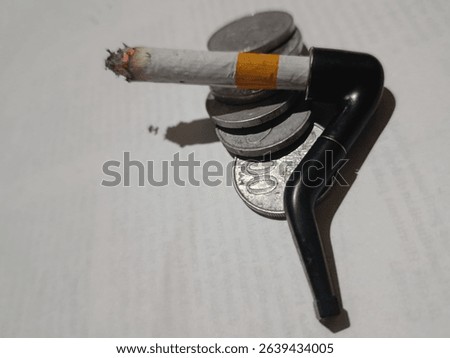 This striking image captures a unique intersection of traditional and modern smoking elements, set against a backdrop of stacked Indonesian coins. A lit cigarette, its ember glowing, is ingeniously pl
