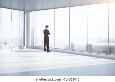 Thoughtful businessman standing in empty room with panoramic windows and New York city view. 3D Rendering