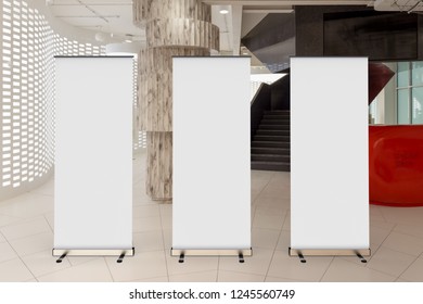 Three Blank Roll Up Banner Stand In Office Interior With Reception Desk And Stairs. Clipping Path Around Ad Banner. 3d Illustration