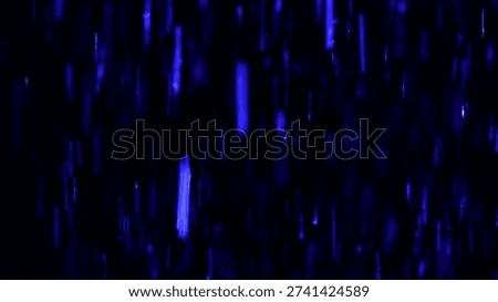 Tiny snow or dust randomly flying in the smoky air, empty space template for objects advertisement. Many dust particles cloud of white powder in blue light on empty dark black contrast background.