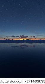 A tranquil 3d Rendering of a star-filled sky over jagged mountains and a glassy lake at dusk.