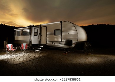 Travel trailer at dusk  with a bright yellow sunset behind a silhouetted ridgeline with trees Ilustrasi Stok